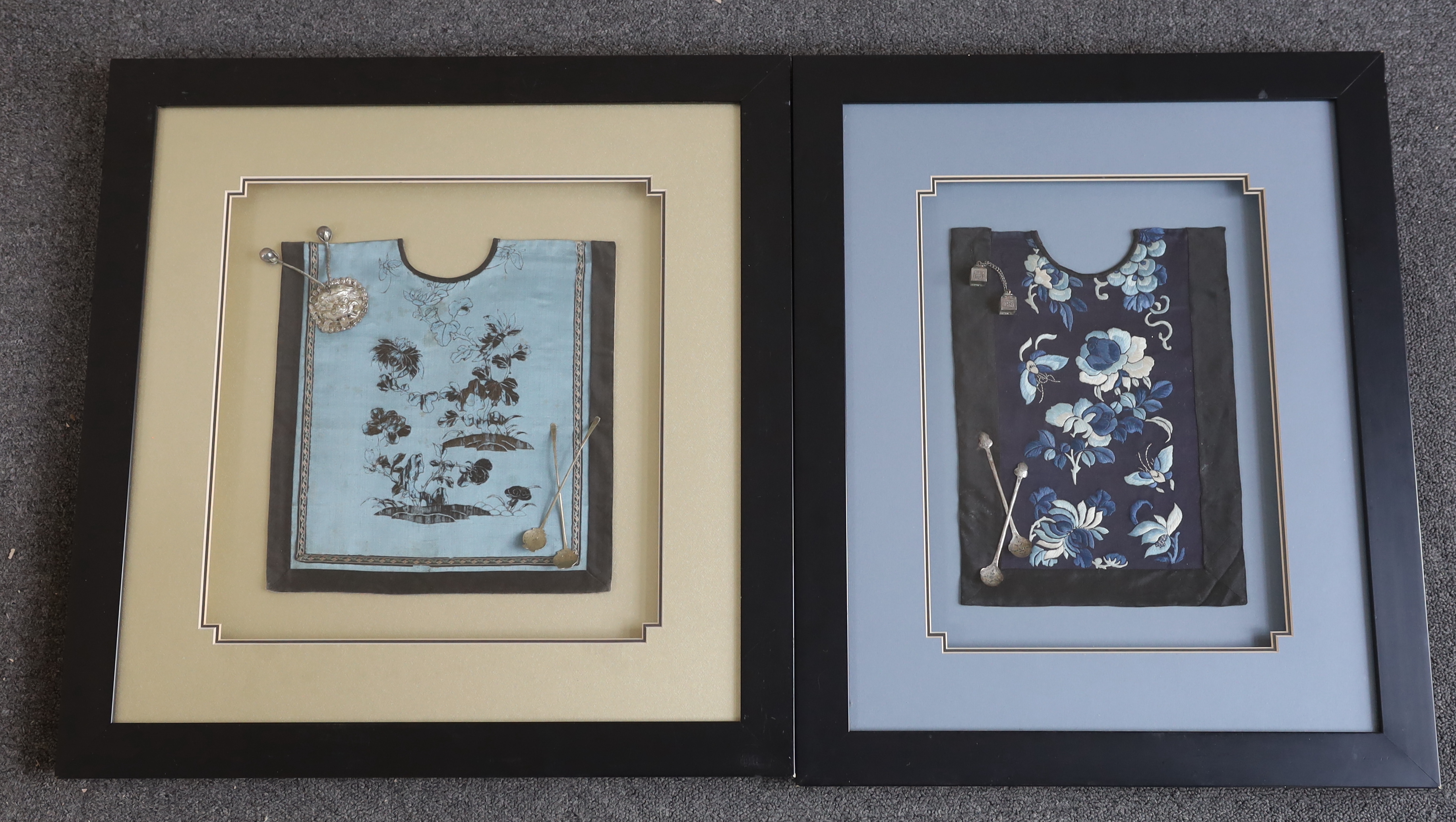 A late 19th century Chinese silk and blue floral embroidered baby’s bib, mounted with two white metal spoons and a rattle, together with a similar bib and spoons plus a decorative white metal mask mount, blue embroidery